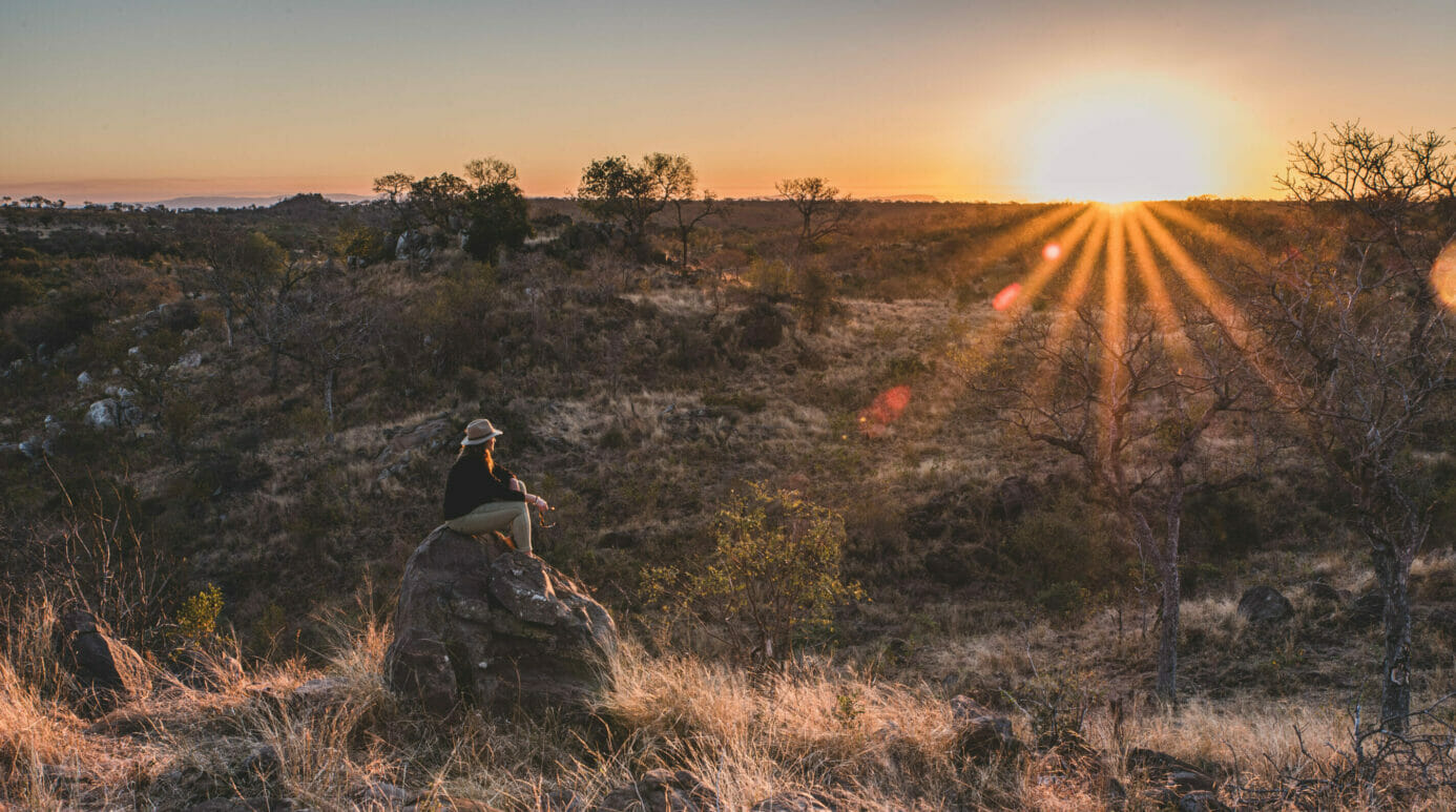 Person sitting on a boulder watching the sunset over the landscape, a sense of wanderlust and space