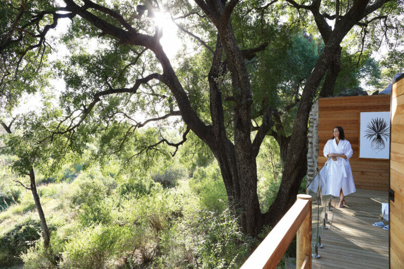 Guest of Londolozi Healing House Retreat standing in white robe on a wooden deck overlooking a canopy of trees.