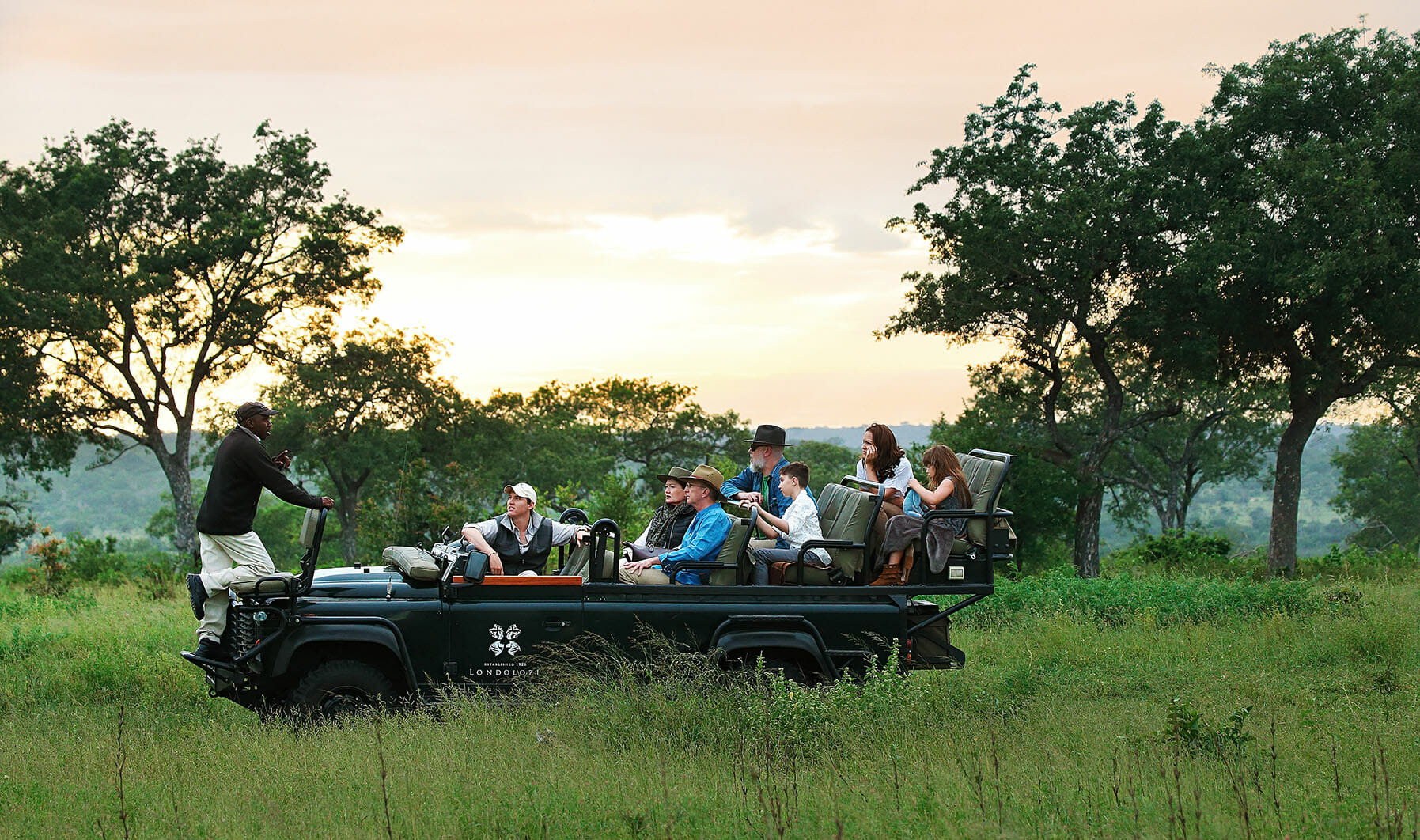 A Land Rover on safari, people listening to ranger and tracker, lush and green, safari experience