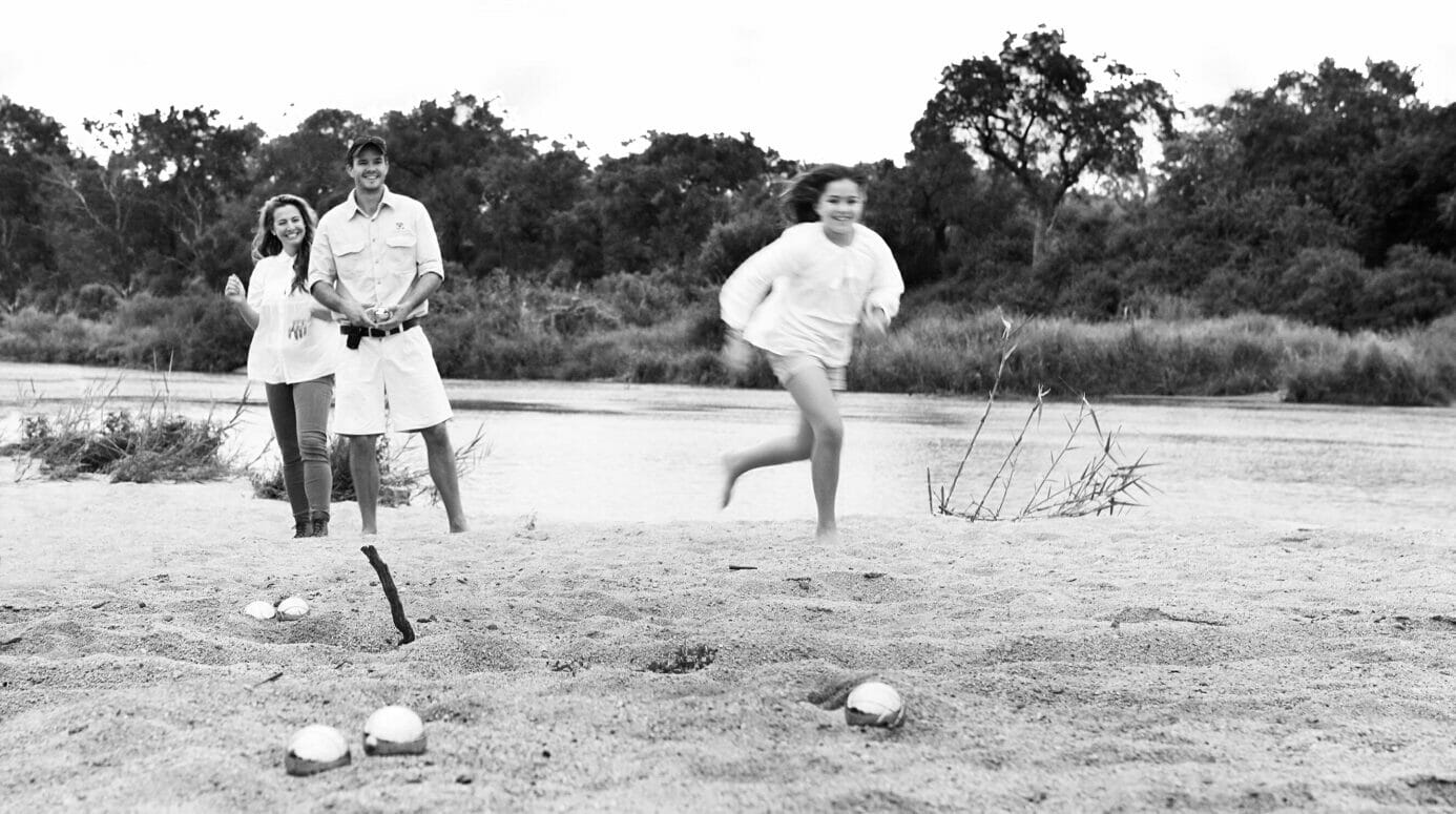 Mother, father and teenager playing bowling on a sandy river bank on a luxury family safari at Londolozi.
