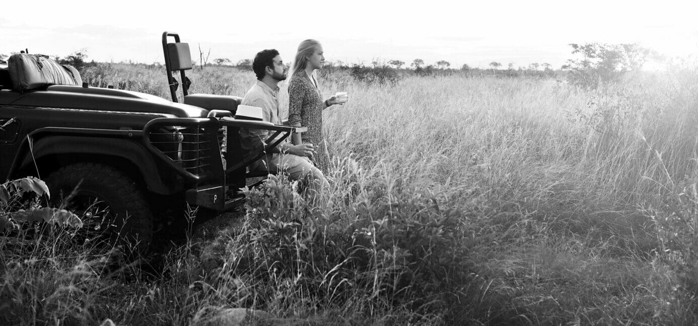 Couple on honeymoon standing in front of a safari vehicle in the wilderness at Londolozi