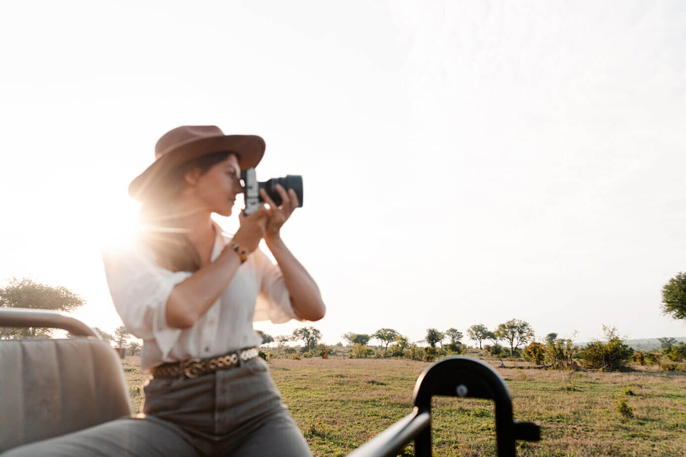 Lady on a safari vehicle taking a picture with grass and trees in the background